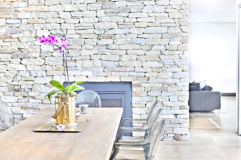Sillas transparentes combinadas con una mesa de madera y la pared de piedra blanca.