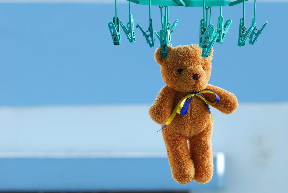 A teddy bear hanging from clothespins to dry.